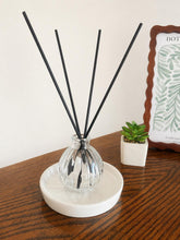 Daisy Blue Home Fragrance Elara Reed Diffuser bottle on a living room shelf with decorative plants and cozy decor.